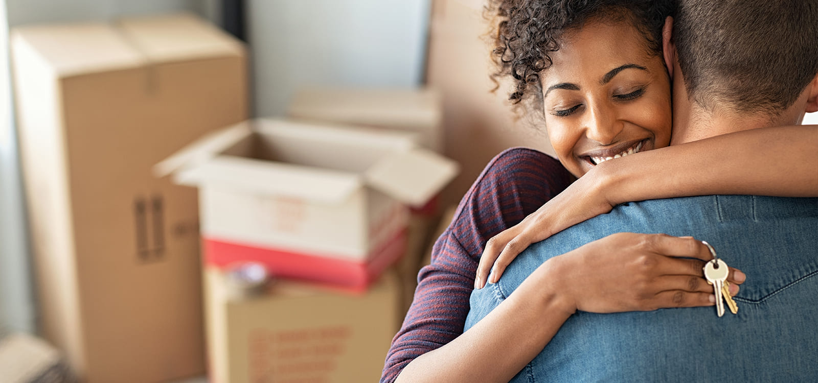 couple hugging with keys in hand and moving boxes in background