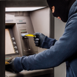 Person in hoodie and black mask skimming money at an ATM.