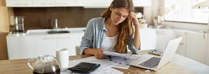 Stressed looking woman looking at paperwork in front of a laptop and calculator