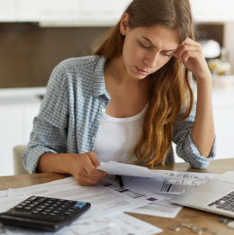 Stressed looking woman looking at paperwork in front of a laptop and calculator