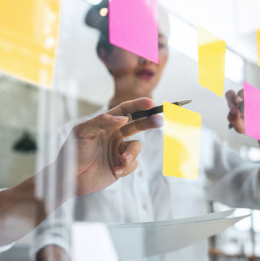 Two people working with sticky notes on a clear board