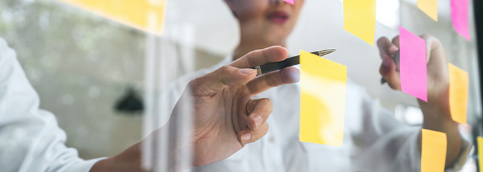 Two people working with sticky notes on a clear board